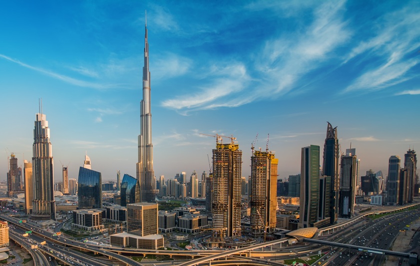 W sercu jednej z najszybciej rozwijających się metropolii świata wznosi się obiekt, który śmiało można nazwać współczesnym cudem architektury – Burdż Chalifa. Ten wieżowiec to nie tylko najwyższy budynek na świecie, ale i manifest technologicznych możliwości człowieka w XXI wieku. Symbol Dubaju, wizytówka Zjednoczonych Emiratów Arabskich i prawdziwa perła współczesnego urbanizmu. To miejsce, które z dnia na dzień zmieniło panoramę miasta i trwale wpisało się w jego tożsamość. W niniejszym artykule przybliżymy historię powstania tego giganta, jego parametry, funkcje, styl architektoniczny oraz znaczenie kulturowe. ________________________________________ Co to jest Burdż Chalifa i gdzie się znajduje? Burdż Chalifa (Burj Khalifa) to wieżowiec mieszczący się w centralnej części Dubaju, w prestiżowej dzielnicy Downtown Dubai. Wzniesiony został jako część wielkiej inwestycji deweloperskiej, mającej na celu przekształcenie pustynnego miasta w światową stolicę luksusu i innowacji. Budynek łączy w sobie wiele funkcji – od przestrzeni biurowych, przez luksusowe apartamenty, aż po ekskluzywny hotel. Znajdują się w nim także restauracje, platformy widokowe oraz centra konferencyjne. Ta różnorodność sprawia, że Burdż Chalifa to swoiste „miasto w chmurach”, samowystarczalna jednostka w strukturze miasta. ________________________________________ Kto zaprojektował Burdż Chalifa? Kulisy współpracy gigantów Za projekt wieżowca odpowiada renomowana amerykańska firma architektoniczna Skidmore, Owings & Merrill (SOM). Głównym projektantem został Adrian Smith, a za konstrukcję odpowiedzialny był Bill Baker – uznawany za jednego z najwybitniejszych inżynierów konstrukcyjnych na świecie. Inspiracją dla kształtu budynku była forma kwiatu Hymenocallis, znanego ze swojej symetrycznej struktury i delikatnej elegancji. To właśnie ten biologiczny wzorzec wpłynął na trójramienną strukturę wieżowca, która zapewnia zarówno estetykę, jak i niespotykaną stabilność przy ekstremalnych wysokościach. ________________________________________ Parametry techniczne – najwyższy budynek świata od stóp do czubka Wysokość Burdż Chalifa budzi podziw – mierzy aż 828 metrów i posiada 163 kondygnacje użytkowe oraz liczne poziomy techniczne. Konstrukcja opiera się na rdzeniu wspartym przyporami (tzw. buttressed core), co zapewnia odporność na wiatr i trzęsienia ziemi. Wieżowiec wyposażony jest w 57 wind, z których niektóre poruszają się z prędkością nawet 10 m/s. Poniższa tabela przedstawia kluczowe parametry budynku: Parametr Wartość Wysokość całkowita 828 m Liczba kondygnacji 163 użytkowe + poziomy techniczne Całkowita powierzchnia ok. 309 000 m² Ilość wind 57 Najszybsza winda ok. 10 m/s Głębokość fundamentów 50 m Beton użyty do budowy ponad 330 000 m³ Ta potęga technologii powstała z myślą o maksymalnym wykorzystaniu przestrzeni i minimalizacji wpływu na środowisko naturalne. Systemy klimatyzacji odzyskują kondensat wody z powietrza, co pozwala zebrać nawet 15 milionów litrów rocznie, wykorzystywanych do nawadniania pobliskiej zieleni. ________________________________________ Etapy budowy – projekt, który przekraczał granice inżynierii Budowa Burdż Chalifa to opowieść o determinacji, precyzji i odwadze – projekt ten dosłownie i metaforycznie wspiął się na wyżyny ludzkich możliwości. Prace konstrukcyjne rozpoczęły się w styczniu 2004 roku, a cała operacja trwała ponad pięć lat, kończąc się oficjalnym otwarciem w styczniu 2010 roku. Od samego początku było jasne, że nie będzie to zwykły wieżowiec. Zespół inżynierów stanął przed wyjątkowymi wyzwaniami – od kwestii strukturalnych i aerodynamicznych po ekstremalne warunki pogodowe w Dubaju. Najbardziej newralgiczne etapy budowy odbywały się nocą, by uniknąć niebezpiecznych temperatur, które za dnia przekraczały 45°C. Beton wylewano jedynie nocą, a do jego mieszania używano specjalnych lodowych granulek, aby utrzymać właściwą temperaturę i uniknąć pęknięć konstrukcyjnych. W szczytowym okresie realizacji na placu budowy pracowało jednocześnie nawet 12 tysięcy ludzi z ponad 100 krajów, co czyniło ją jednym z najbardziej wielokulturowych projektów inżynieryjnych w historii. Wznoszenie Burdż Chalifa odbywało się w tempie około 1–2 pięter tygodniowo, co przy tej skali było imponującym wyczynem. Specjalnie zaprojektowane pompy do betonu były w stanie wtłaczać materiał na wysokość ponad 600 metrów – to rekord w tej dziedzinie. Równolegle prowadzono prace nad wykończeniem wnętrz, instalacją systemów HVAC, wind i elementów wykończeniowych – wszystko z chirurgiczną precyzją i przy użyciu najnowszych dostępnych technologii. Burdż Chalifa to dowód na to, że marzenia architektów i inwestorów, oparte na naukowej wiedzy i technologii, mogą przerodzić się w rzeczywistość, nawet jeśli wydają się z pozoru niemożliwe. Proces budowy Burdż Chalifa był ogromnym przedsięwzięciem logistycznym: • Zastosowano beton wysokowytrzymałościowy, który był wylewany głównie w nocy ze względu na ekstremalne temperatury w Dubaju. • Korzystano z zaawansowanych technologii monitoringu wiatru, co pozwalało planować kolejne etapy konstrukcyjne. • Współpracowały setki firm z różnych krajów, a liczba pracowników sięgała 12 000 osób dziennie w szczytowym okresie. ________________________________________ Styl architektoniczny – neofuturyzm z nutą tradycji Choć Burdż Chalifa to szczyt nowoczesnego designu, jego forma nie jest przypadkowa ani wyłącznie efektem estetyki. Budynek reprezentuje neofuturyzm – nurt architektoniczny, który łączy zaawansowaną technologię z wizją przyszłości. Jego struktura to również odzwierciedlenie islamskiej sztuki geometrycznej, widocznej w planie trójramiennej podstawy. Iglicowy kształt symbolizuje duchowe dążenie ku górze, a jednocześnie zapewnia aerodynamiczne właściwości pozwalające zminimalizować wpływ wiatru. ________________________________________ Funkcje użytkowe – Burdż Chalifa jako pionowe miasto Ten kolos nie jest pustą ikoną – pełni wiele praktycznych funkcji: • Hotel Armani – zajmuje piętra od 1 do 8 oraz 38–39, zaprojektowany przez samego Giorgio Armaniego. • Luksusowe apartamenty mieszkalne – rozmieszczone od 19 do 108 piętra. • Powierzchnie biurowe – najwyższej klasy przestrzenie komercyjne. • Platformy widokowe – dostępne dla turystów, w tym popularne: o „At the Top” (124. piętro) o „Sky” (148. piętro) o najwyższy punkt widokowy świata na 154. piętrze • Restauracje i przestrzenie rekreacyjne – w tym ekskluzywna „At.mosphere” na 122. piętrze. Wizja Burdż Chalifa nie kończy się na imponującej bryle – to obiekt o wielofunkcyjnym charakterze, zaprojektowany tak, by tworzyć zintegrowaną przestrzeń miejską w pionie. Nie jest to wyłącznie biurowiec ani hotel, lecz całościowy ekosystem, który łączy w sobie funkcje mieszkaniowe, komercyjne, turystyczne i rekreacyjne. Najniższe piętra, od 1 do 8 oraz 38–39, zajmuje luksusowy Hotel Armani, zaprojektowany we współpracy z Giorgio Armanim. To miejsce, gdzie elegancja i nowoczesność spotykają się w przestrzeniach z panoramicznym widokiem na miasto. Wyżej, od 19. do 108. piętra, rozciągają się ekskluzywne apartamenty mieszkalne, które oferują nie tylko luksusowe wnętrza, ale także dostęp do prywatnych siłowni, basenów i sal klubowych. Piętra 112–154 przeznaczono na powierzchnie biurowe klasy A+, zarezerwowane dla największych globalnych marek i firm z sektora finansów, nowych technologii i doradztwa. Warto dodać, że wszystkie te przestrzenie zaprojektowano z uwzględnieniem najwyższych standardów energooszczędności i komfortu użytkownika. Na szczególną uwagę zasługują tarasy widokowe, które znajdują się na 124., 148. i aż 154. piętrze – to one przyciągają setki tysięcy turystów rocznie. Każdy z nich oferuje inny poziom doświadczeń: od podstawowego „At the Top” po ekskluzywne „Sky Lounge”, gdzie goście mogą podziwiać zachód słońca z kieliszkiem szampana w dłoni. Całość uzupełniają restauracje, centra konferencyjne oraz strefy rekreacyjne, czyniąc Burdż Chalifa prawdziwym „miastem w chmurach”, w którym można mieszkać, pracować i wypoczywać bez potrzeby opuszczania budynku.________________________________________ Rekordy i ciekawostki – Burdż Chalifa na tle świata Nie sposób mówić o Burdż Chalifa bez wspomnienia o licznych rekordach, które ten wieżowiec bije na każdym kroku. Jest to najwyższy budynek świata, ale także obiekt o największej liczbie kondygnacji, najdłuższej trasie pokonywanej przez windę i najwyżej położonym tarasie widokowym. Jego 828 metrów wysokości to wynik, który do dziś nie został pobity przez żaden inny ukończony budynek. Jednak to nie jedyne fascynujące fakty, które kryją się za jego fasadą. Restauracja „At.mosphere”, mieszcząca się na 122. piętrze, jest uznawana za najwyżej położoną restaurację na świecie – serwuje ekskluzywne dania kuchni fusion w oprawie panoramicznej panoramy Dubaju. Windy Burdż Chalifa przemierzają z kolei najdłuższy pionowy dystans w historii architektury – ponad 504 metry, a do tego poruszają się z zawrotną prędkością 10 metrów na sekundę. Warto także wspomnieć o mniej oczywistych rekordach. Na szczycie wieżowca zamontowano najwyżej położony system konserwacji elewacji, który pozwala na mycie szyb z pomocą specjalnych platform przesuwanych po prowadnicach. Co ciekawe, całkowite mycie wszystkich szyb budynku trwa 3 miesiące, a po jego zakończeniu trzeba... zacząć od początku. Burdż Chalifa to także częsty bohater kultury masowej – pojawił się m.in. w hollywoodzkim hicie „Mission: Impossible – Ghost Protocol”, gdzie Tom Cruise osobiście wspinał się po jego szklanej elewacji bez użycia kaskadera. Budynek ten jest też sceną największych pokazów fajerwerków i świateł na świecie, szczególnie w noc sylwestrową. Wtedy fasada zamienia się w gigantyczny ekran LED, a Dubaj staje się centrum uwagi całego globu. Te wszystkie elementy sprawiają, że Burdż Chalifa to nie tylko rekordowy budynek, ale też żywa, dynamiczna przestrzeń kulturowa i technologiczna, która wciąż ewoluuje i inspiruje kolejne pokolenia. Wieżowiec z Dubaju bije rekordy i budzi wyobraźnię: • Najwyższy budynek świata – od momentu otwarcia do dziś. • Najwyżej położony taras widokowy – 555 metrów nad ziemią. • Najwyższa restauracja świata – „At.mosphere” na 122. piętrze. • Najwyższy punkt konserwacji budynku – specjalne platformy serwisowe umożliwiają mycie szyb na niebotycznych wysokościach. • Najdłuższy dystans pokonywany przez windę – aż 504 metry. Burdż Chalifa pojawił się także w filmach, reklamach i grach komputerowych. Szczególnie głośna była scena z udziałem Toma Cruise’a w „Mission: Impossible – Ghost Protocol”, gdzie aktor wspina się po szklanej elewacji budynku. ________________________________________ Znaczenie kulturowe i turystyczne – symbol aspiracji Dubaju Dla mieszkańców Dubaju i całego świata arabsko-perskiego Burdż Chalifa jest symbolem siły, ambicji i nowoczesności. Budynek stanowi kluczowy punkt w krajobrazie turystycznym miasta, przyciągając rocznie miliony gości. Każdego roku odbywają się tu spektakularne pokazy fajerwerków na Sylwestra, transmitowane przez stacje telewizyjne na całym świecie. Ponadto, cały kompleks Downtown Dubai, z fontannami i centrum handlowym Dubai Mall, tworzy unikalne doświadczenie miejskie. ________________________________________ Podsumowanie – Burdż Chalifa jako manifest ludzkości Burdż Chalifa to coś więcej niż najwyższy wieżowiec świata. To pomnik współczesnych możliwości inżynieryjnych, manifest ambicji i wizji przyszłości, a także narzędzie miejskiego storytellingu. Pokazuje, jak można połączyć funkcjonalność, technologię i estetykę, tworząc strukturę, która inspiruje – nie tylko architektów, ale także marzycieli i innowatorów na całym świecie.